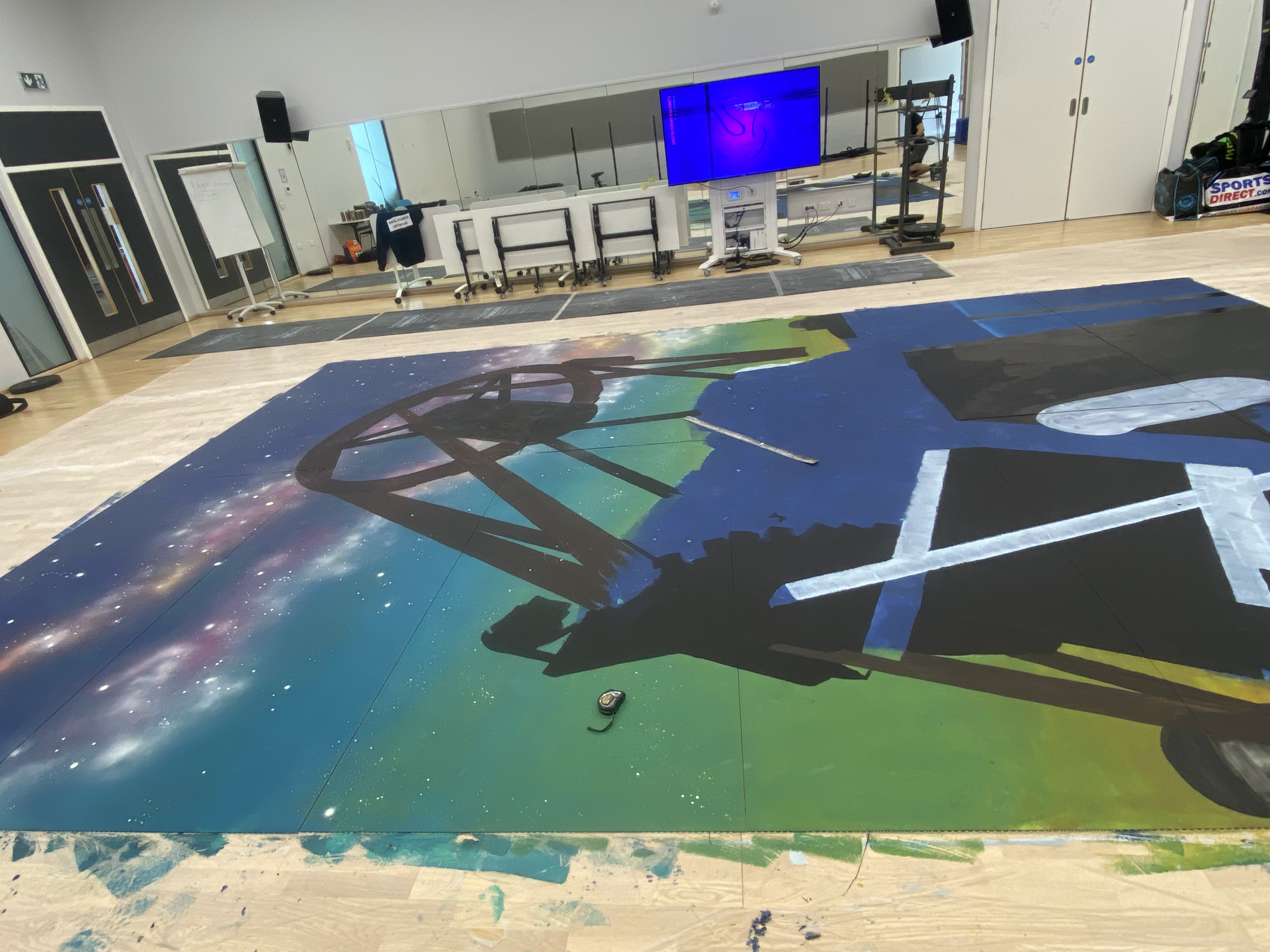 Painting of the LT mural. The mural boards are on the floor of the gym, half painted